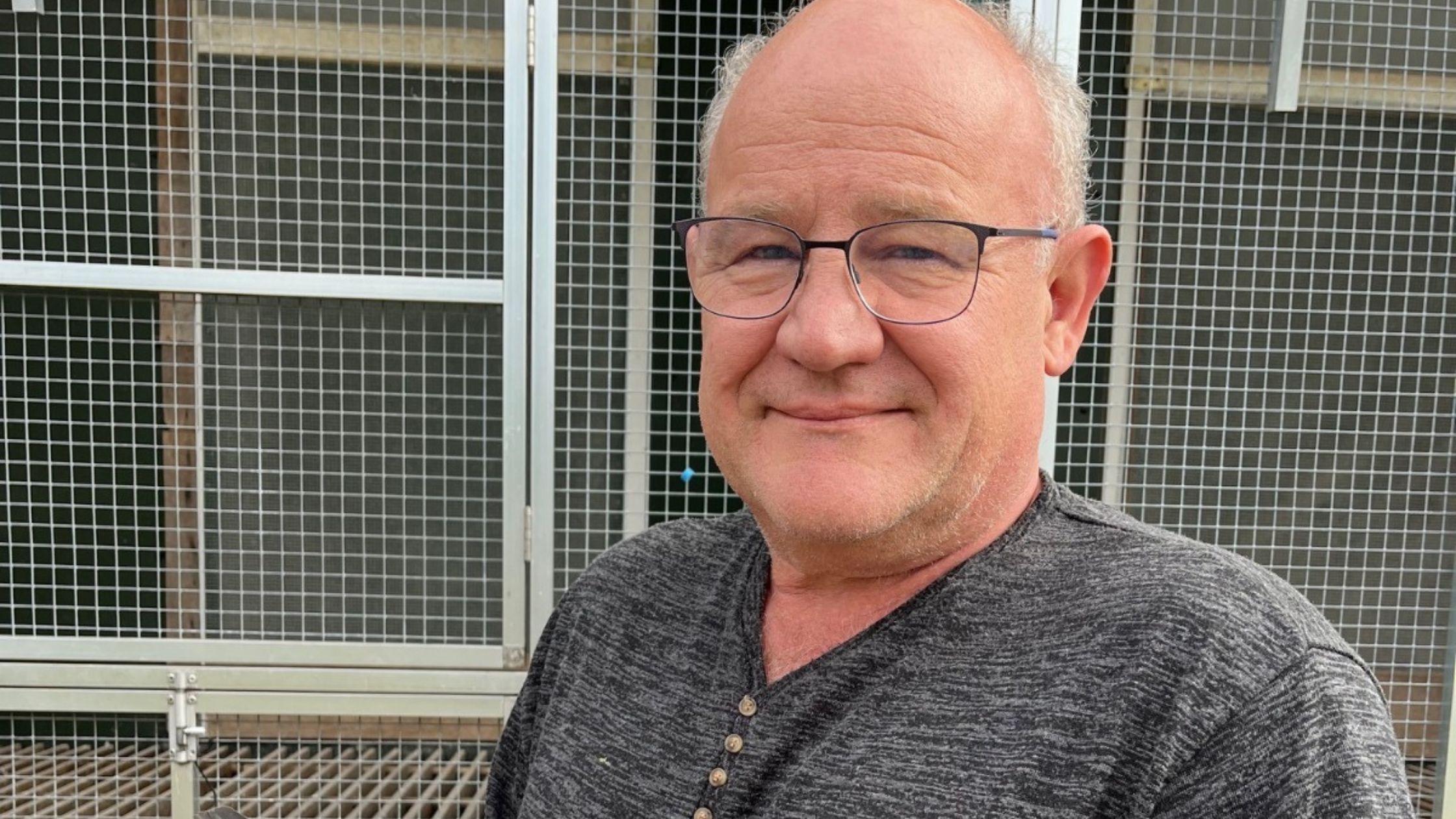 A smiling Huub Hermans, the renowned pigeon fancier from Born, proudly holding his champion racing pigeon, NL.21-1398369 "Mister Teletext", inside his well-structured racing loft.