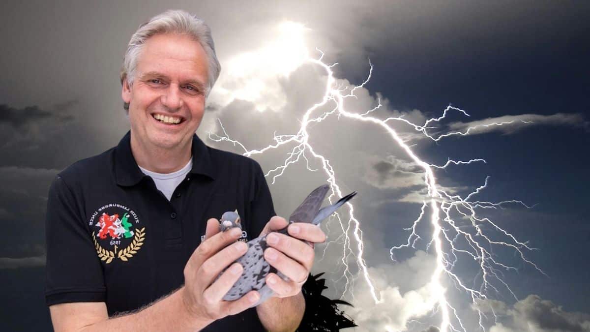 A photograph of pigeon fancier Rex de Leeuw smiling warmly while holding a checkered racing pigeon in his hands. The background features a dramatic sky filled with dark storm clouds and powerful lightning strikes, perfectly illustrating the story of De Leeuw Pigeons braving the intense thunderstorms during the Pau marathon race.