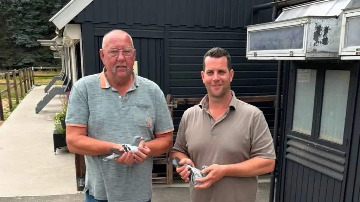 The proud champions of Combination Kroesen standing in front of their modern black pigeon lofts. Both men are passionately holding one of their elite racing pigeons, showcasing the true dedication behind this top sport.