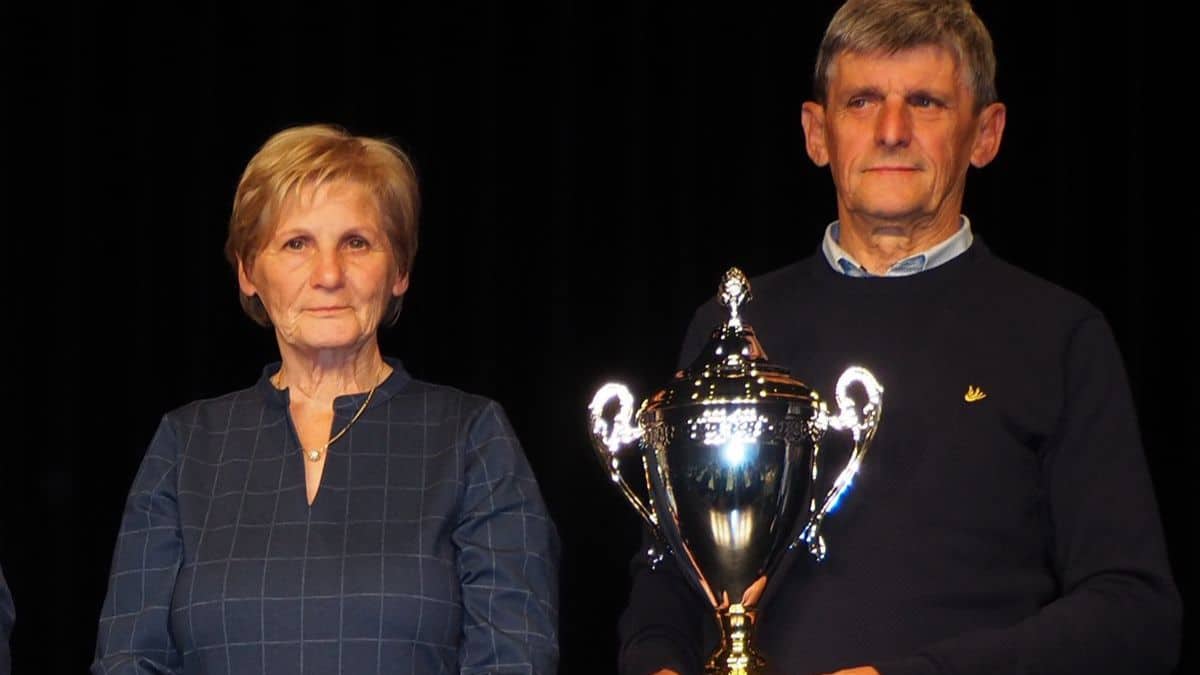 Roger and Godelieve Thys proudly holding a large silver trophy on stage during a national pigeon racing award ceremony.